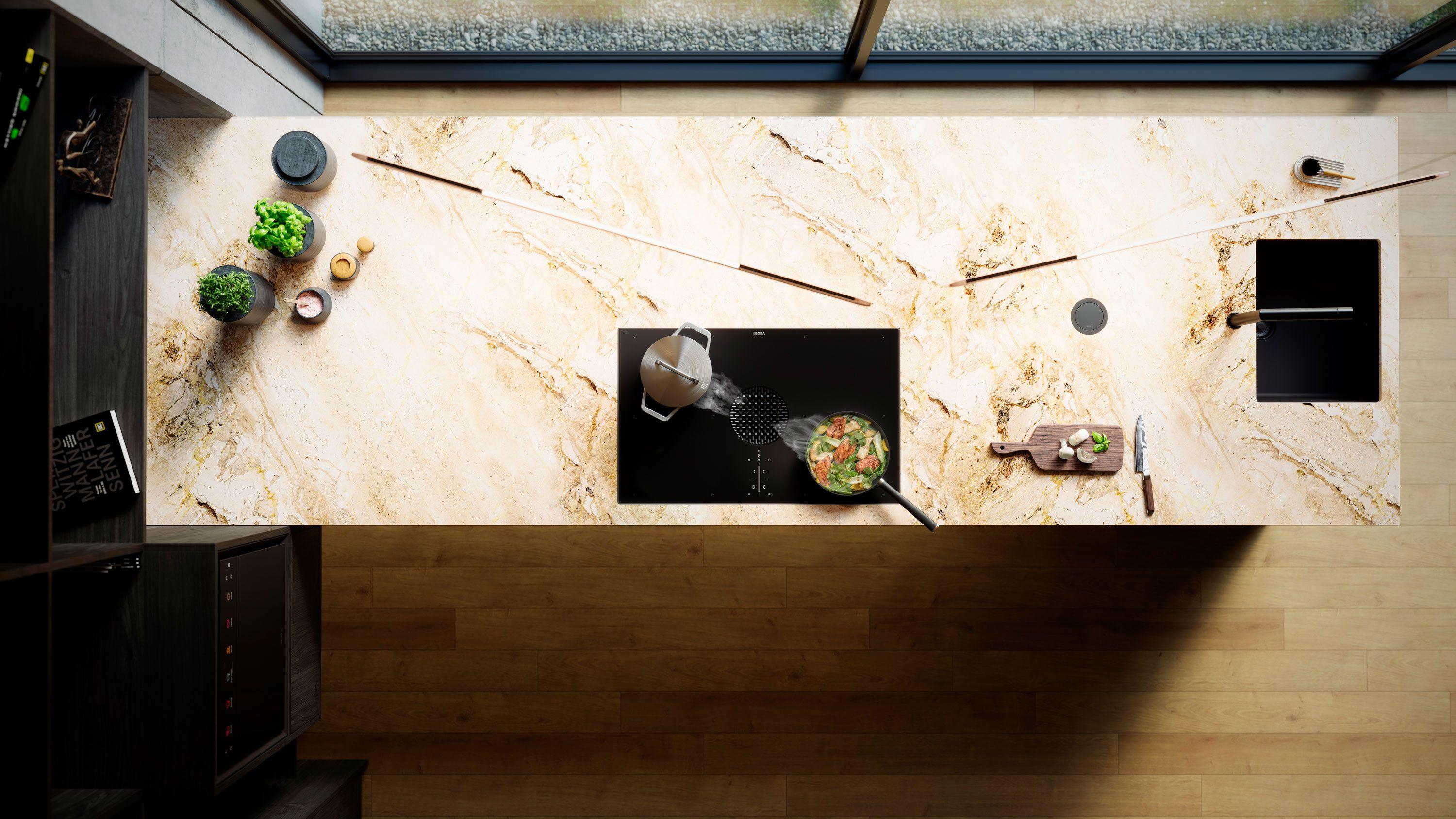 BORA X Pure in der Kücheninsel – Kochfeld mit integriertem Dunstabzug in schwarzem Glas, Topf und Pfanne beim Kochen, Spüle und Zubehör auf heller Natursteinoptik-Arbeitsplatte (Top-Down-Ansicht)