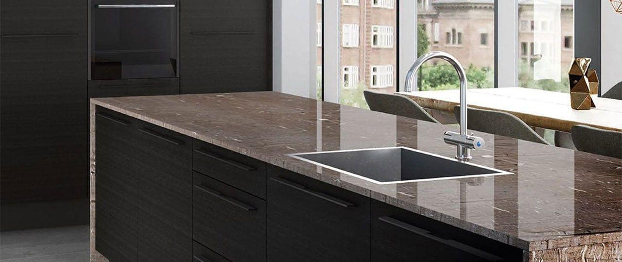 Kücheninsel mit schwarzer Front und glänzender Granit-Arbeitsplatte aus Naturstein; eckige Unterbauspüle mit hoher Chrom-Armatur vor großer Fensterfront und Essplatz im Hintergrund