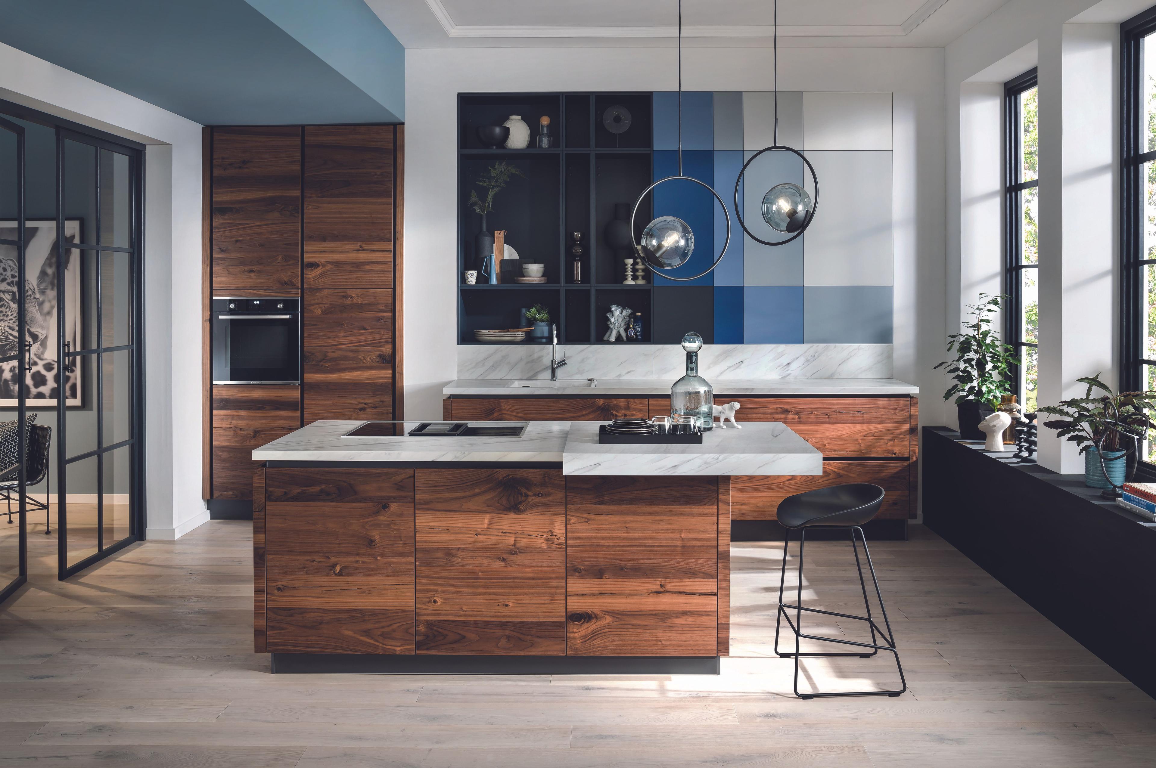 Luxuriöse Häcker Küche mit Nussbaumfronten, Marmorarbeitsplatte und farbigen Designrückwänden.