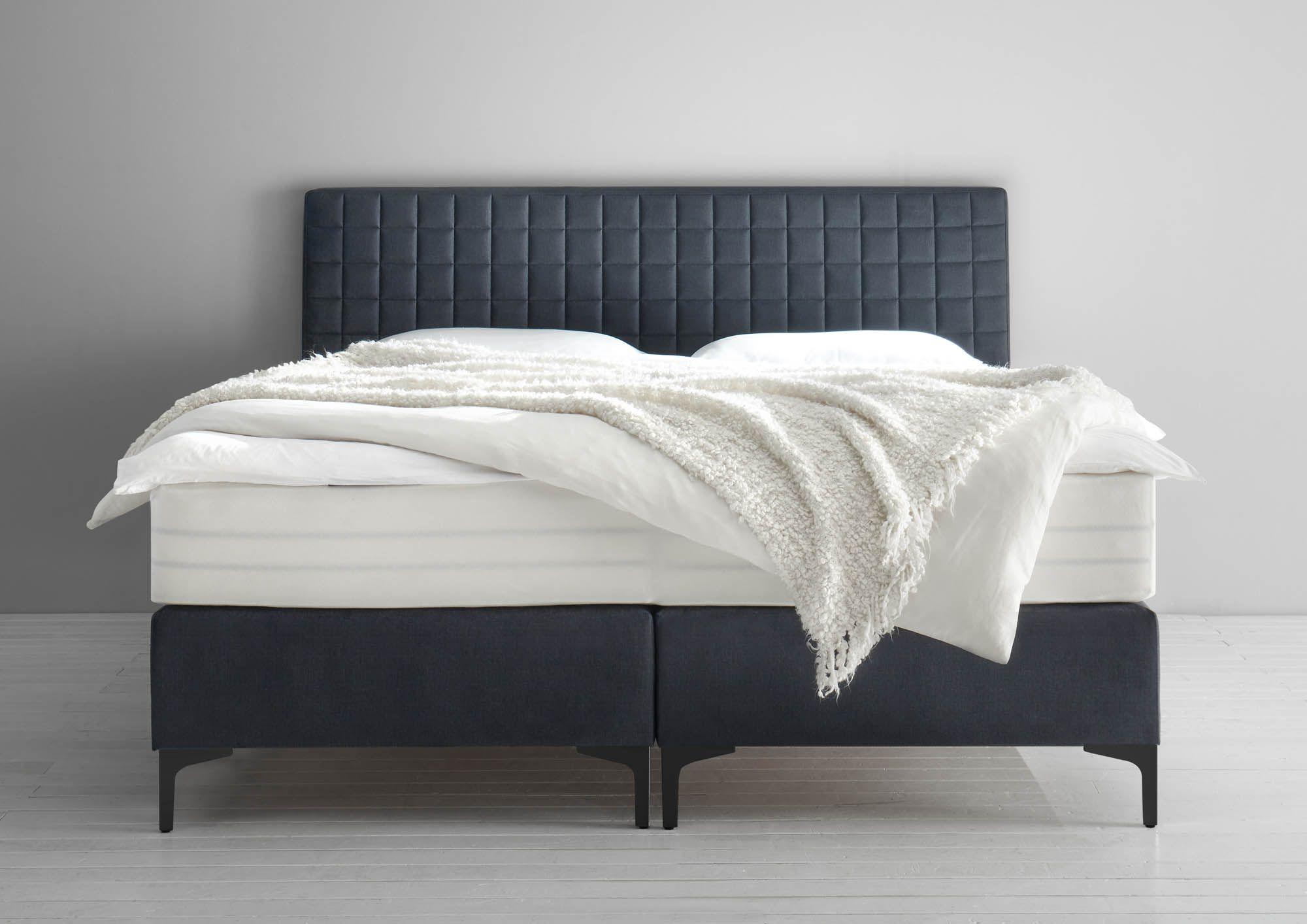 Casada KT 205 Boxspringbett in Anthrazit mit quadratisch gestepptem Kopfteil und weißer Bettwäsche, minimalistisches Design vor grauem Hintergrund