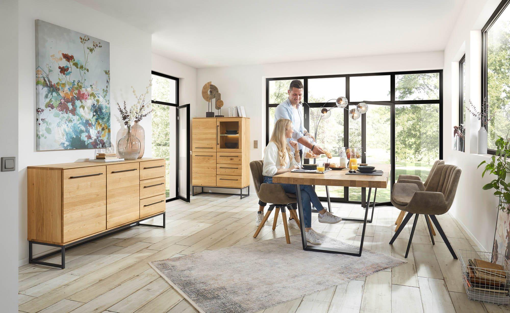 Cascais Wohn- und Esszimmerprogramm in Eiche mit schwarzem Metallgestell – Sideboard, Highboard und Esstisch mit Polsterstühlen, Paar beim Frühstück im lichtdurchfluteten Raum