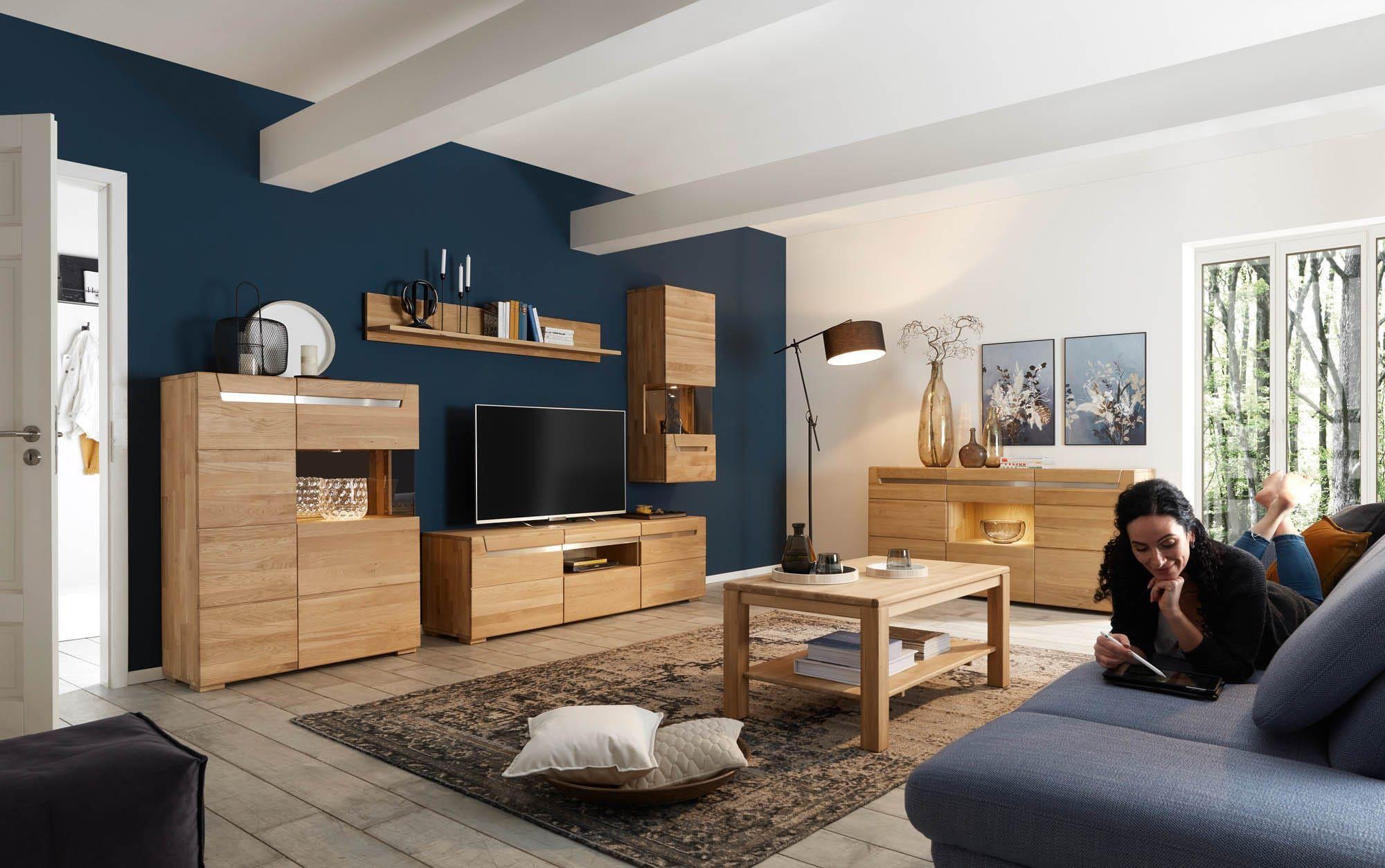 Gemütliches Wohnzimmer mit moderner Wohnwand in Holzoptik: TV-Board, Hängeschrank, Regalböden und Sideboard, kombiniert mit Couchtisch, Sofa und akzentuierter blauer Wandfarbe im hellen Raum