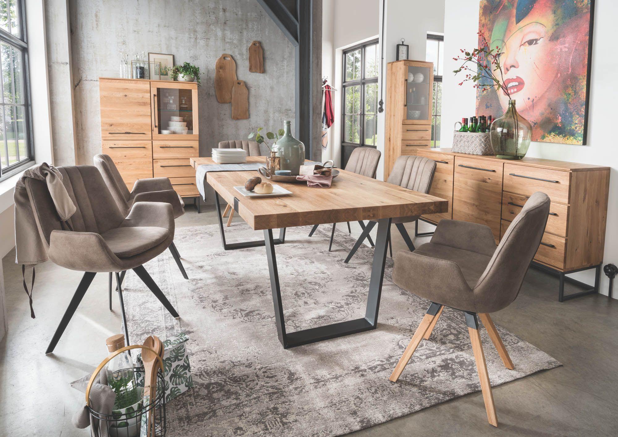 Niehoff Essgruppe in Wildeiche mit Esstisch auf Metallkufen, taupefarbenen Polsterstühlen, Highboard und Sideboard in industriellem Loft-Ambiente mit Betonwand