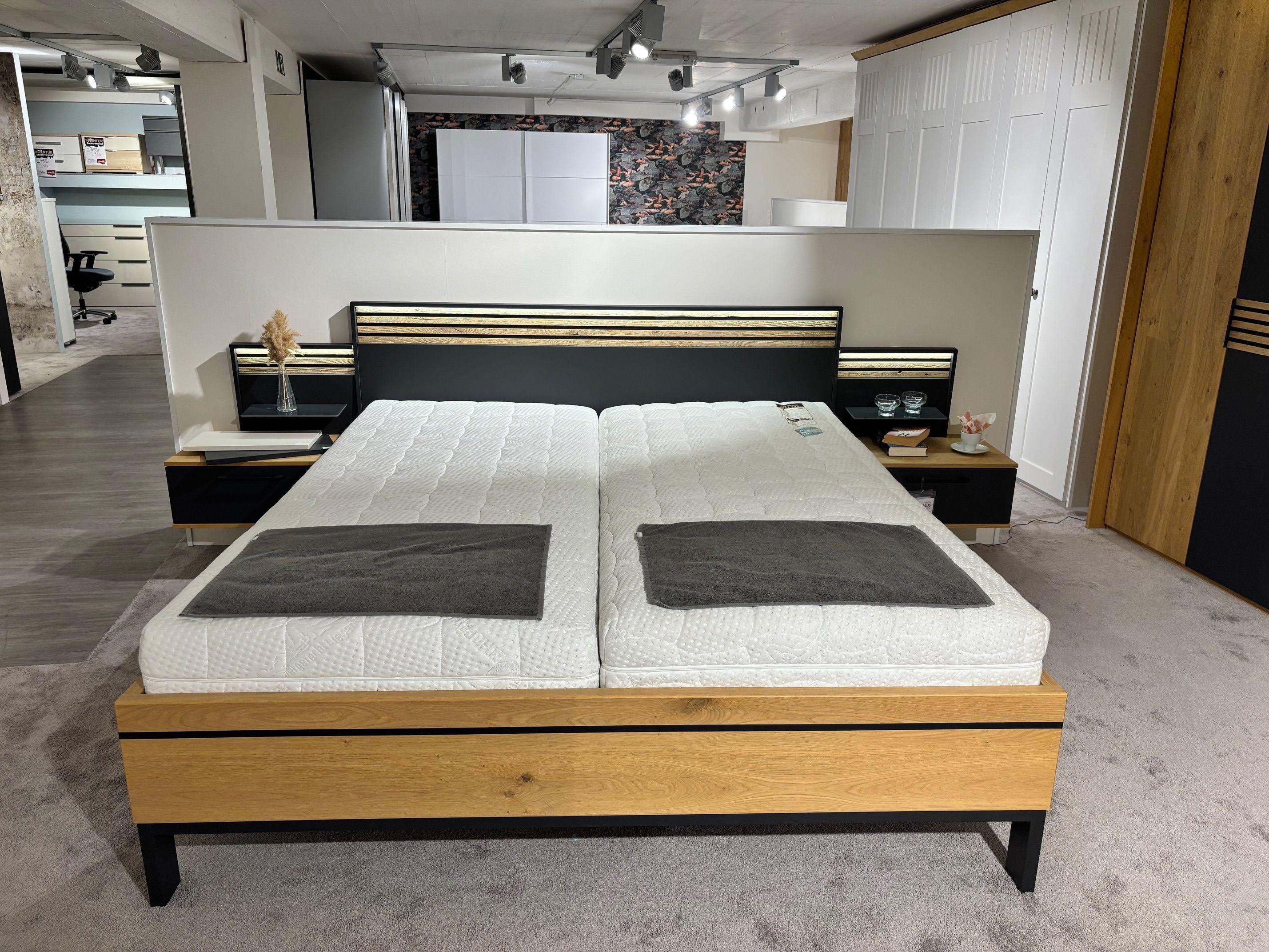 Doppelbett in Eiche und Anthrazit mit beleuchtetem Kopfteil, zwei Matratzen und schwebenden Nachttischen in Frontansicht.