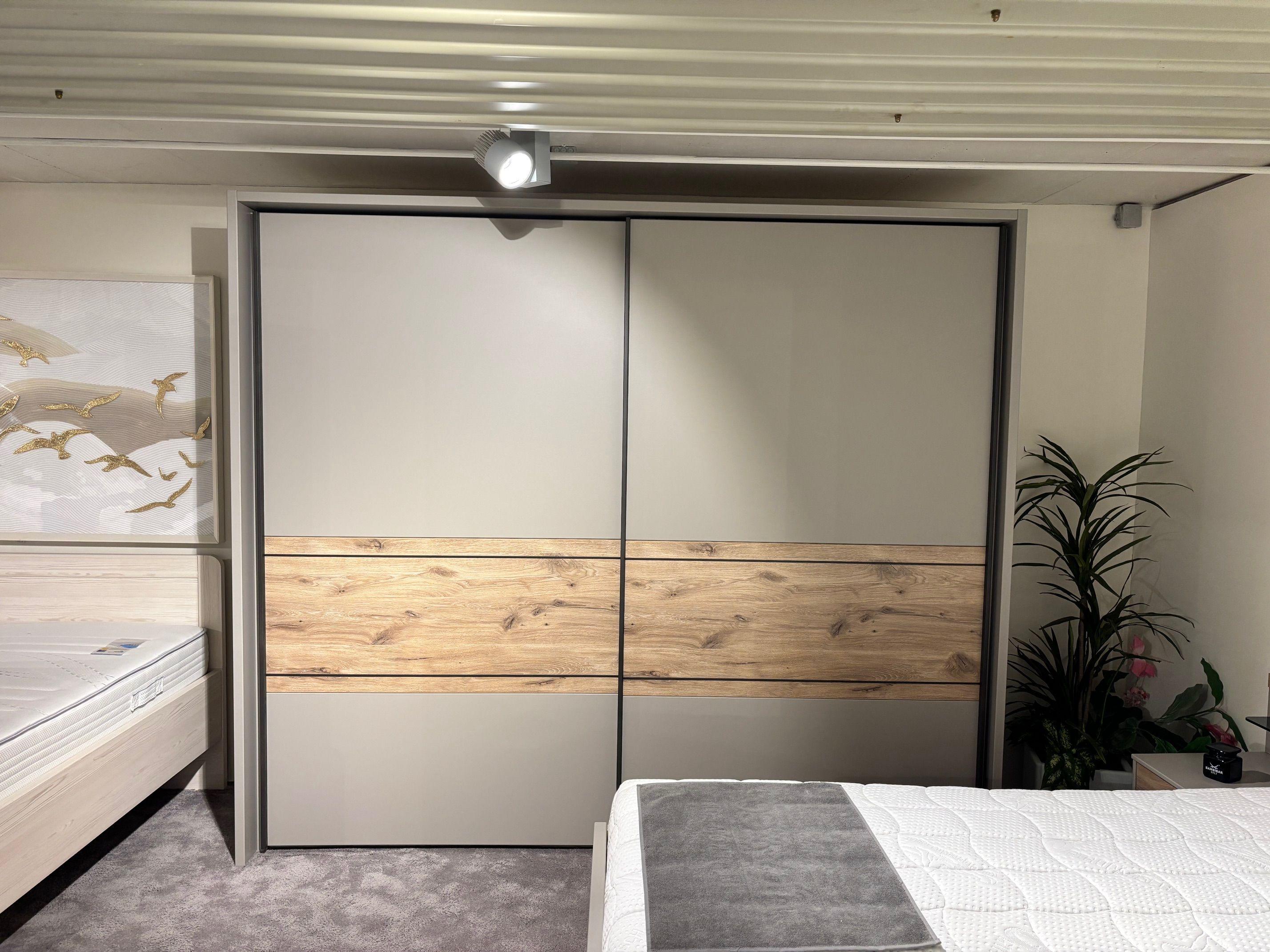 Zweitüriger Schwebetürenschrank in Grau mit breitem Eiche-Dekorband in der Mitte, Gesamtansicht im Showroom.