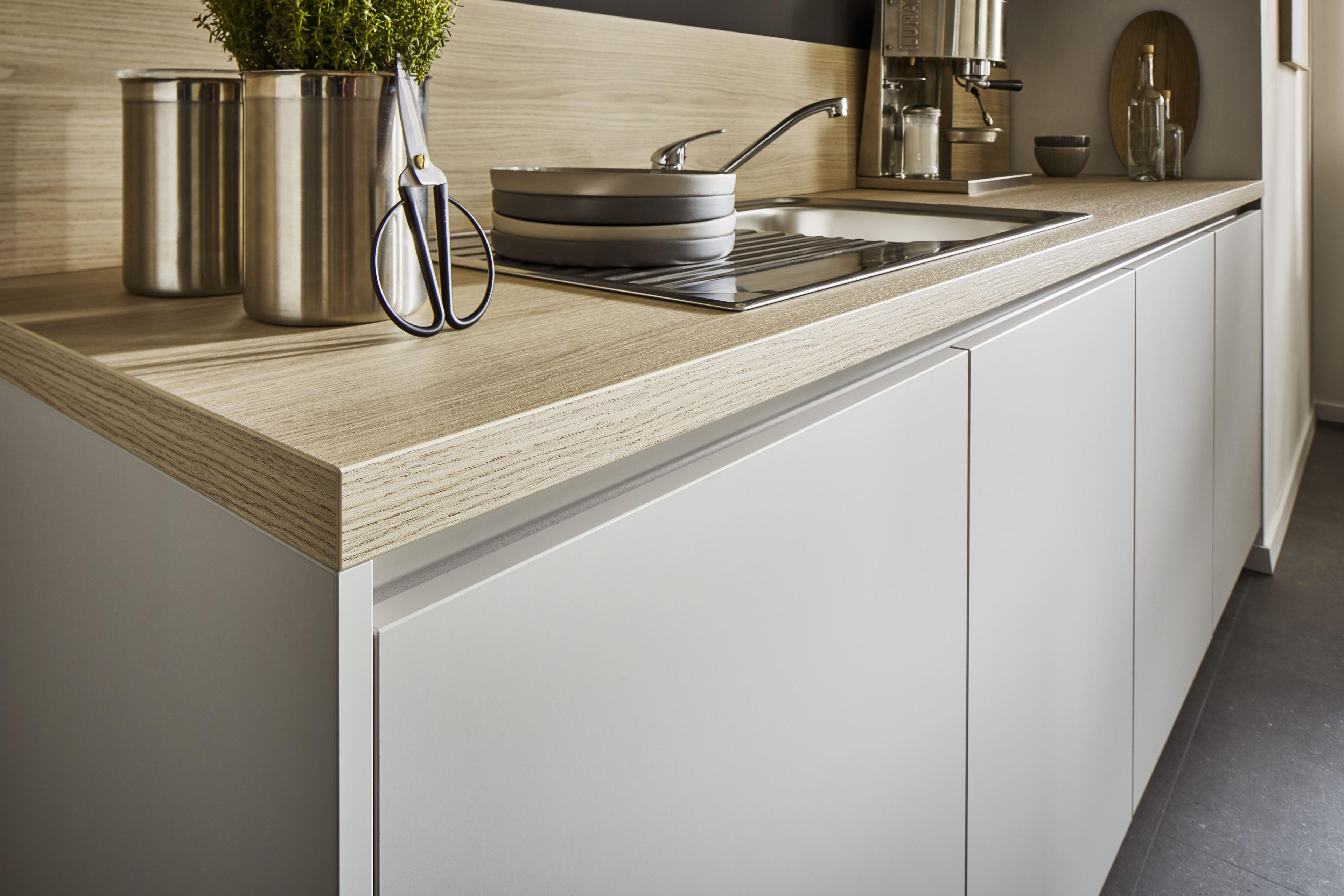 Detailaufnahme einer Häcker Küche mit grifflosen Fronten in Lichtgrau und heller Holzoptik.