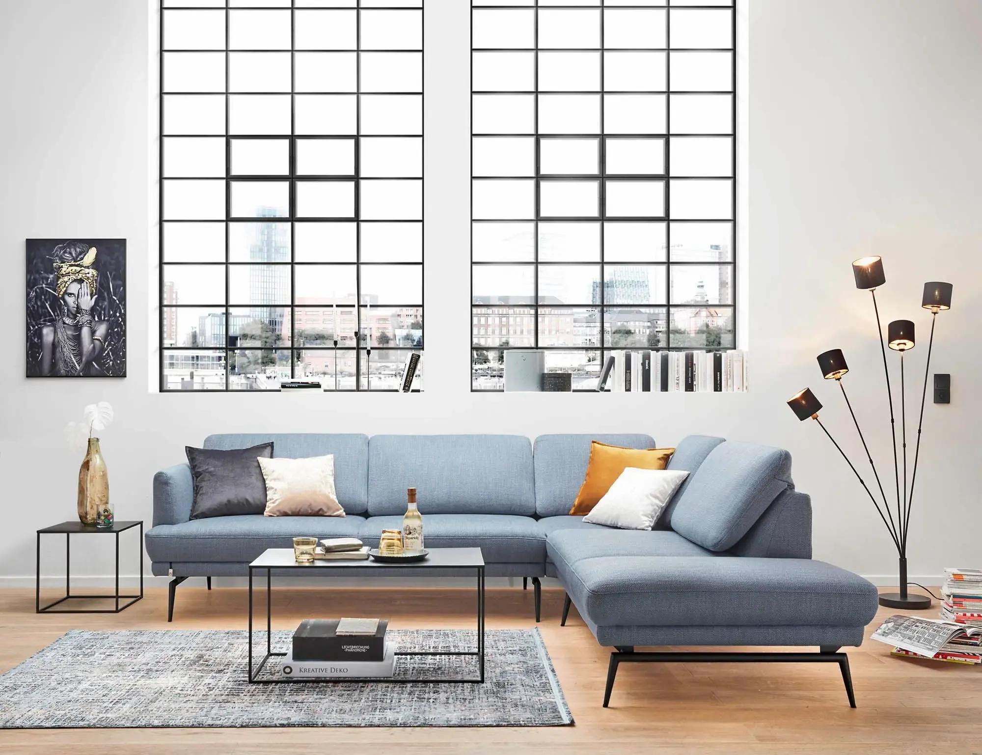 Hellblaues Ecksofa Caruba mit Récamiere in einem lichtdurchfluteten Loft-Wohnzimmer mit Industriefenstern und modernen Accessoires