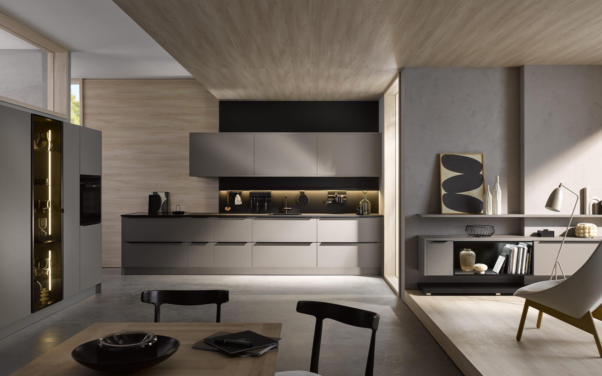 Häcker Küche AV 2042 in Samteiche Greige – minimalistische Designküche mit grifflosen Fronten, dunkler Arbeitsplatte, beleuchteter Nische und Hochschrank-Vitrine; kombiniert mit warmen Holzflächen und modernem Wohnbereich